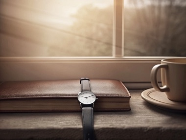 A wristwatch lying on a closed leather book on a windowsill, a cup of tea beside it in cool morning light.